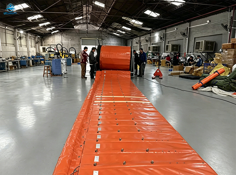 Orange retractable flood barrier being rolled up in factory, showing compact storage design