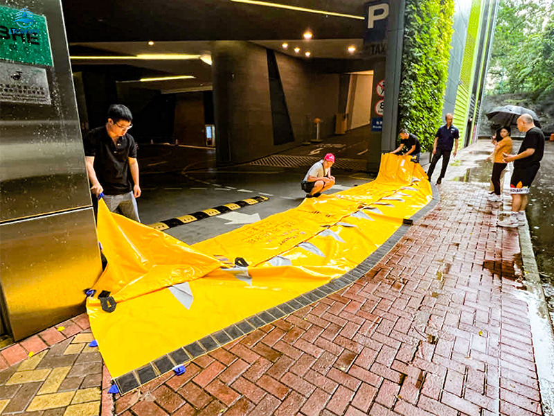 Workers setting up yellow self-rising flood barrier at building entrance