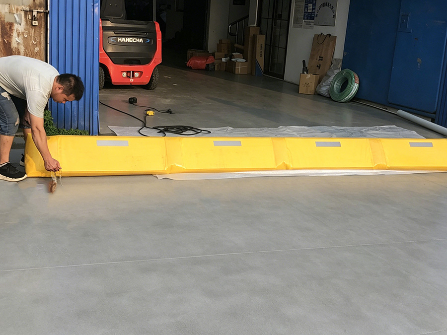 Worker laying yellow reusable water-filled flood barrier at warehouse entrance